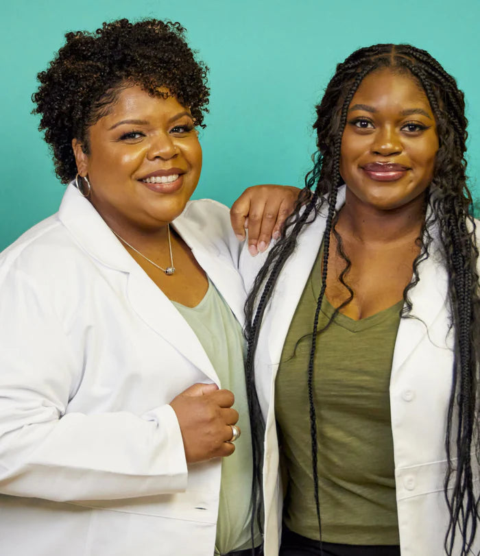 Two USRx employees wearing white lab coats on a light blue background